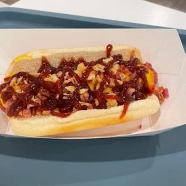 A Funky Franks hot dog with barbecue sauce, cheese, and crispy toppings in a white tray.