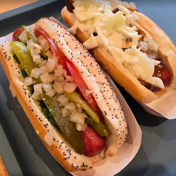 Two Funky Franks hot dogs, one with pickles and tomatoes, the other with coleslaw and onions.