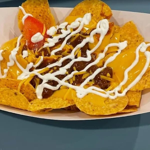 Funky Franks chili cheese nachos with sour cream and a tomato slice in a white tray.
