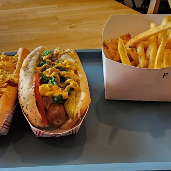 Two Funky Franks hot dogs with various toppings and a side of french fries on a tray.