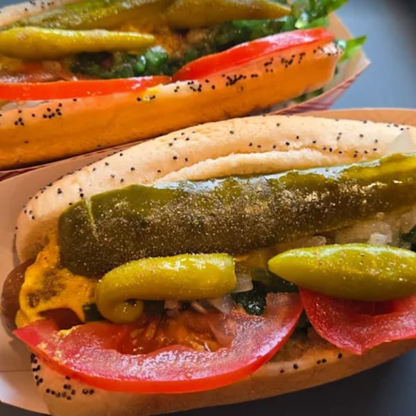 Two Funky Franks hot dogs with mustard, tomatoes, pickles, and green relish in poppy seed buns.