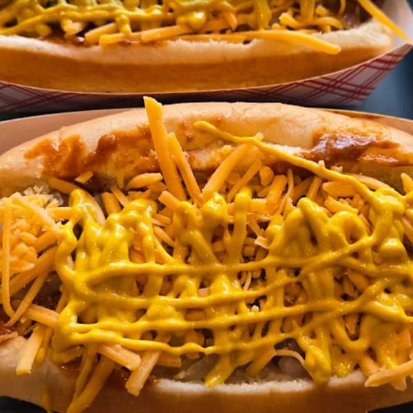 Two Funky Franks hot dogs with chili, shredded cheese, and yellow mustard in paper trays.